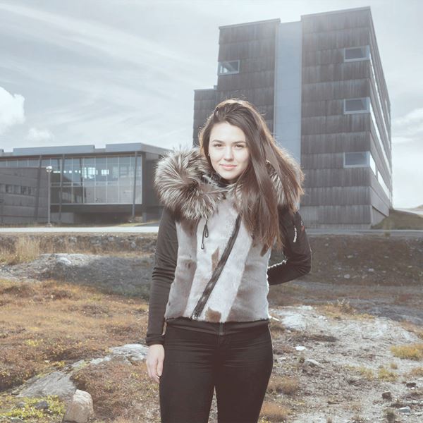 En ung kvinde står udenfor i den grønlandske natur. 