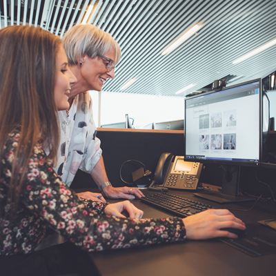 To kvinder ved et kontorbord som kigger ind i en computerskerm.