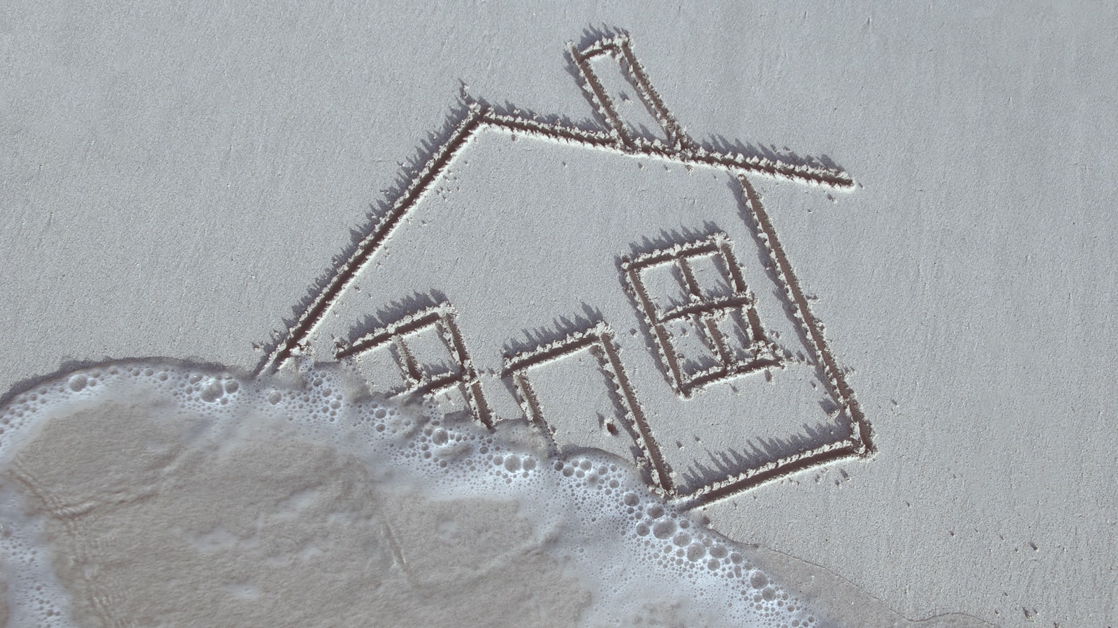 Hus tegnet i sand med vand på vej ind over