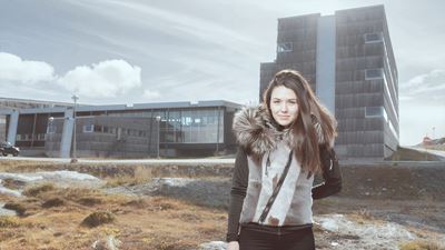 En ung kvinde står udenfor i den grønlandske natur. 