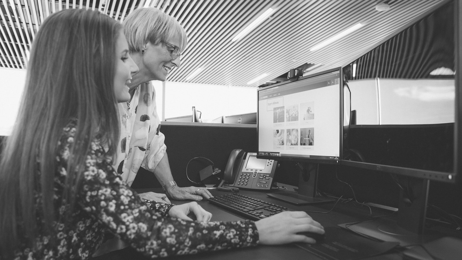 To kvinder ved et kontorbord som kigger ind i en computerskerm.