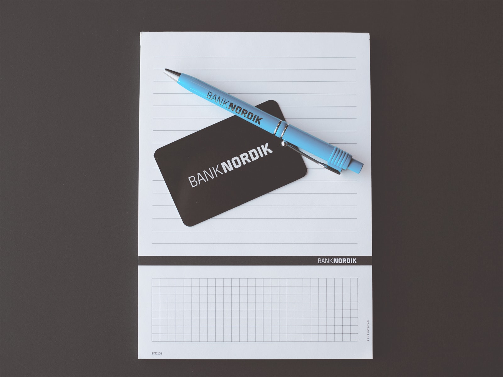 Et Banknordik kort og en blyant liggende på en skriveblok. 