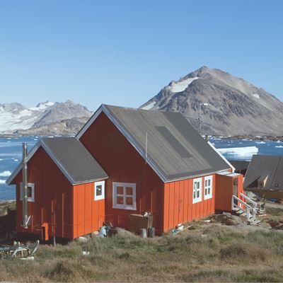 Røde huse med en flot udsigt over vand og bjerge i Grønland. 
