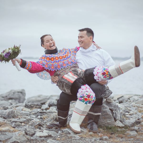 Nygift grønlandsk par i deres nationaltøj sidder på på en sten og kvinden har med blomster i hånden.  