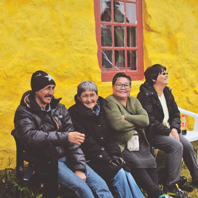 Fire mennesker sidder på en bænk udenfor mod et gul mur. 