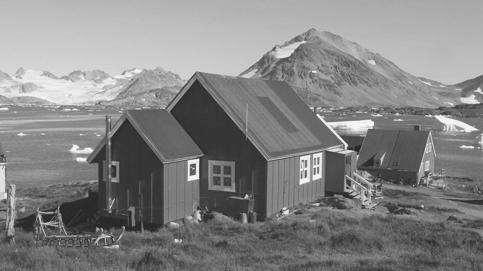 Røde huse med en flot udsigt over vand og bjerge i Grønland. 