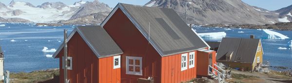 Røde huse med en flot udsigt over vand og bjerge i Grønland. 